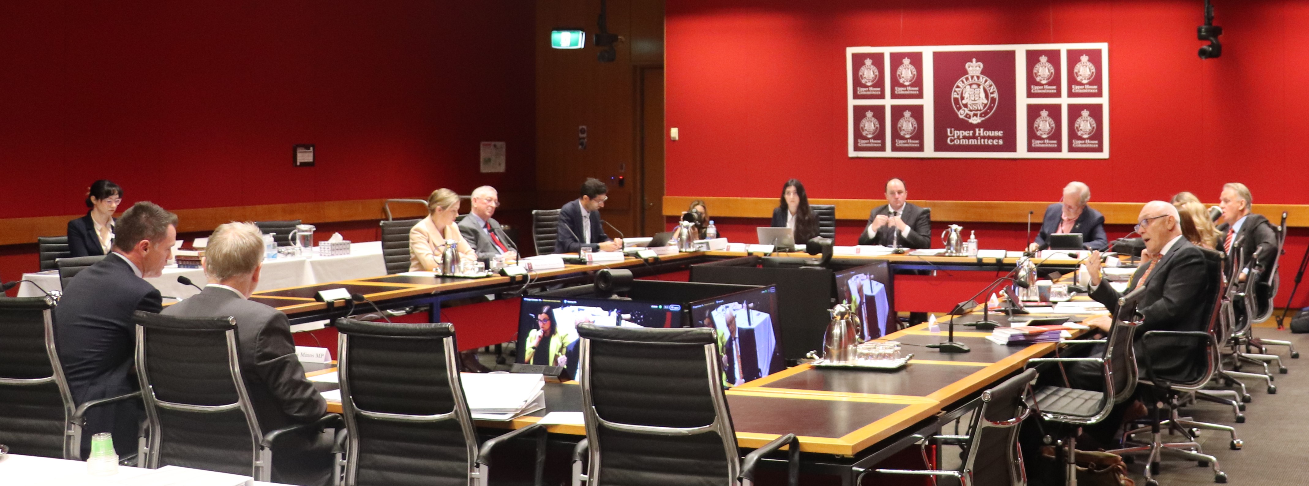 A hearing room with the committee sitting at a table questioning witnesses